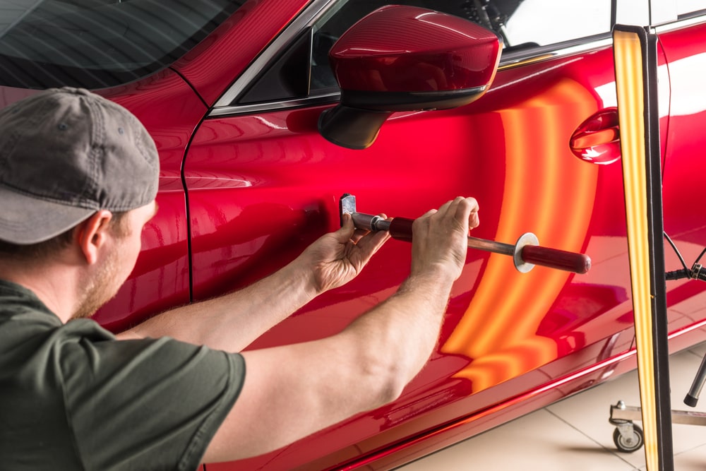 A technician removing dents without painting. Red car with a dent - automotive care.