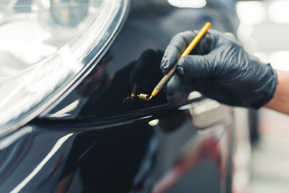 A skilled mechanic in protective gloves precisely touches up small scratches on a car, doing what technicians do with paint touch-ups in New Orleans