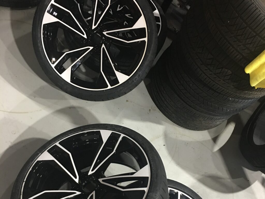 A set of sleek black and white car rims displayed next to a stack of four black tires at Armadillo automotive, a Kenner Automotive Services shop.