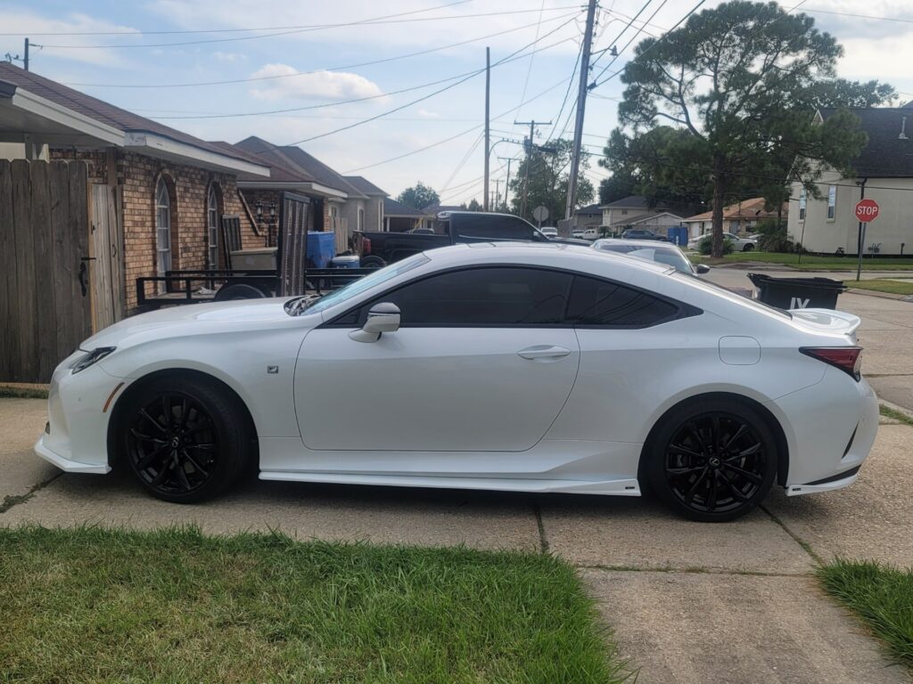 Side profile of a white sports coupe with black rims parked on a suburban street, exemplifying the high-performance of vehicles serviced by Kenner automotive professionals.