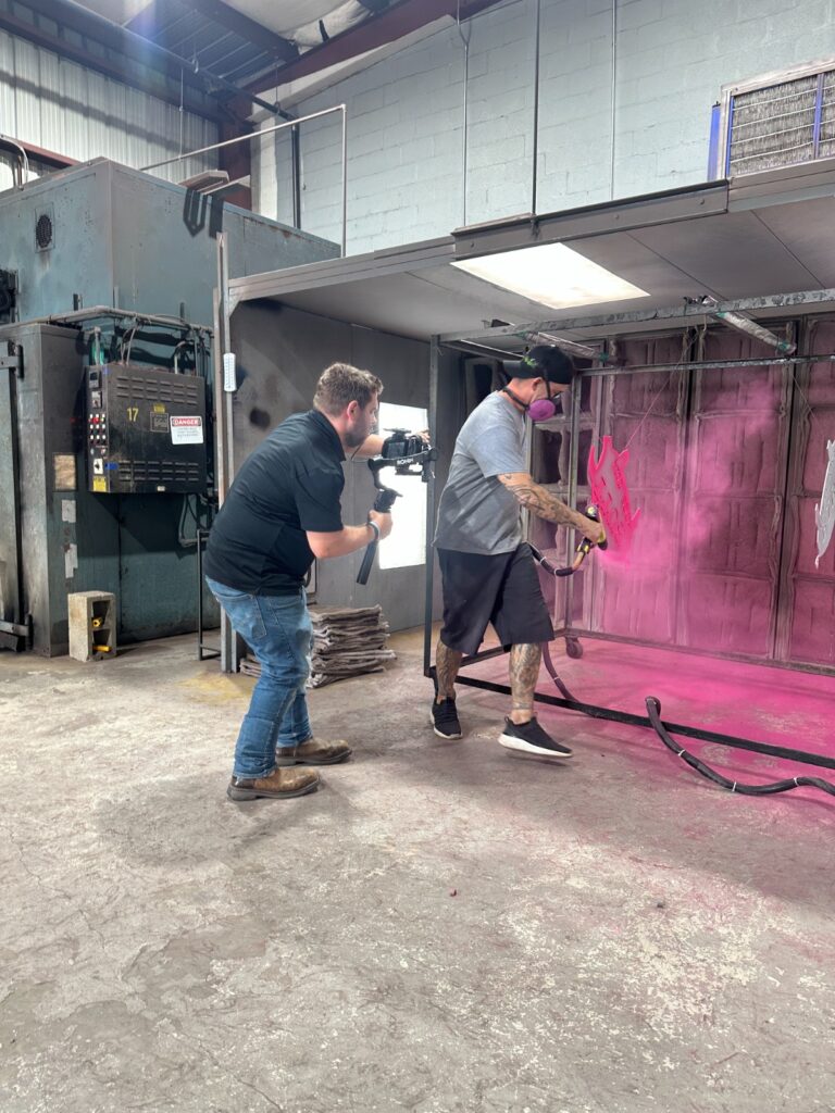 Kenner automotive powder coating process in action, with Armadillo Automotive technician spraying a bright pink coat on pig-shaped metal awards.