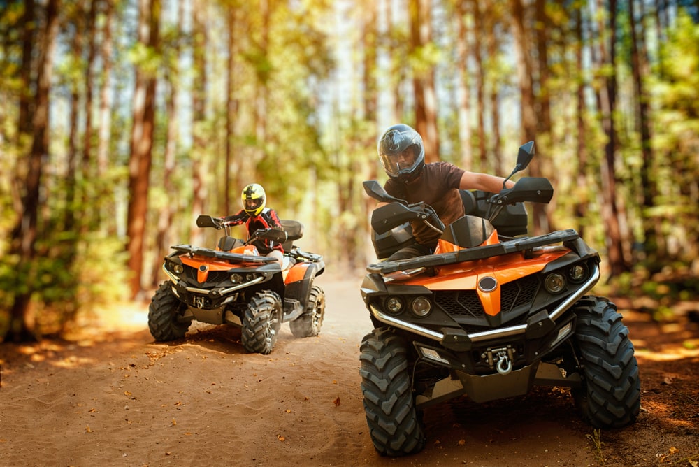 Two quad riders, speed race in forest, front view. Showcasing the importance of quad maintenance. Kenner Automotive.